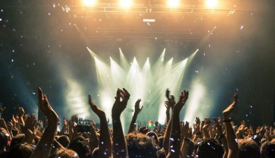 A music concert scene of a crowd with raised hands with a light show on a stage in the background.