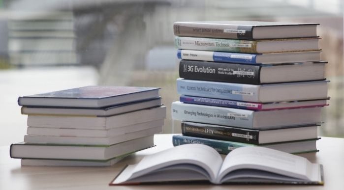 Two piles of books on a desk with an open book in the foreground.