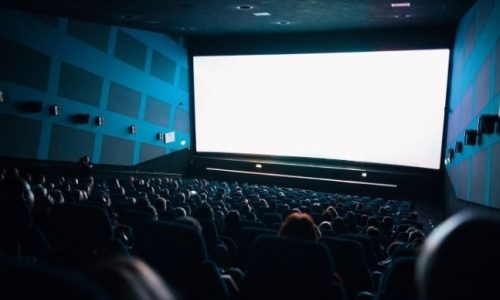 A cinema room with blue walls and an audience seated in front of a blank screen.