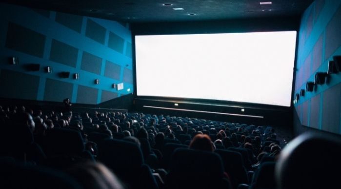 A cinema room with blue walls and an audience seated in front of a blank screen.